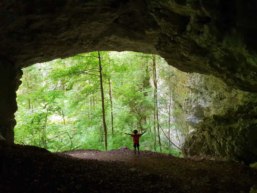 Niño con los brazos abiertos en la entrada de la cueva Krizna, Eslovenia