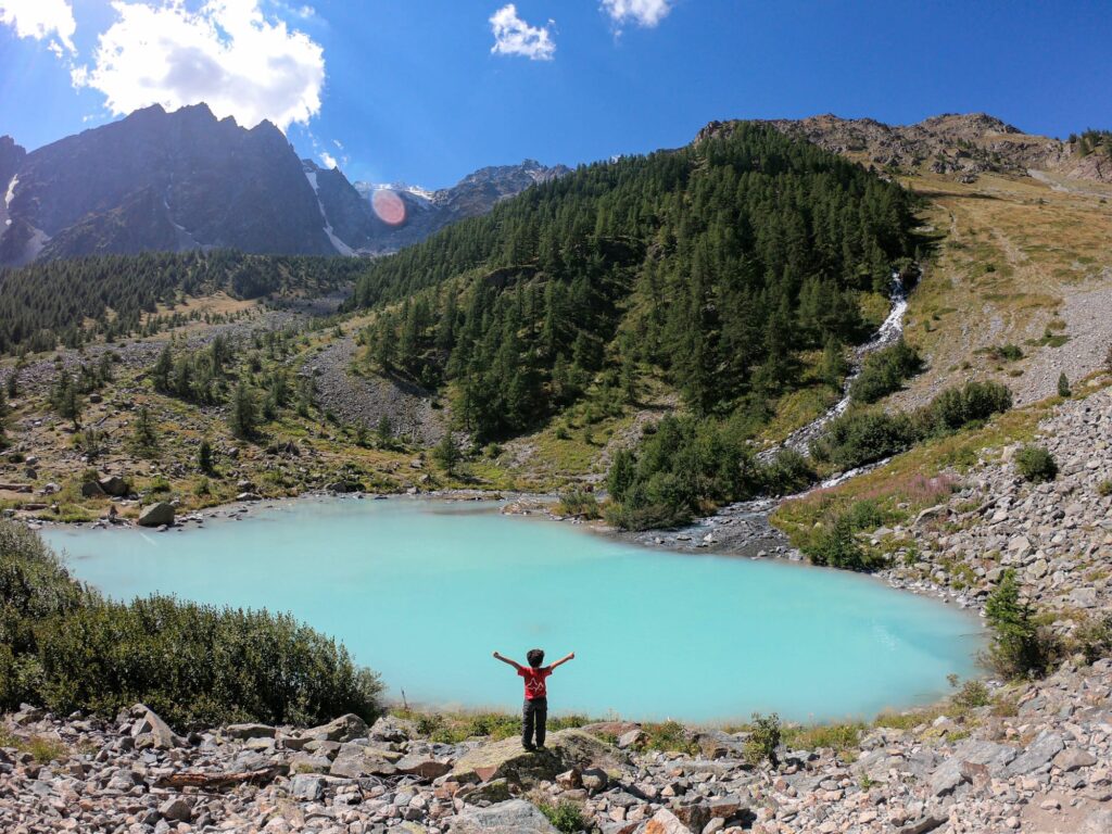 Niño con brazos abiertos frente a un lago turquesa de montaña