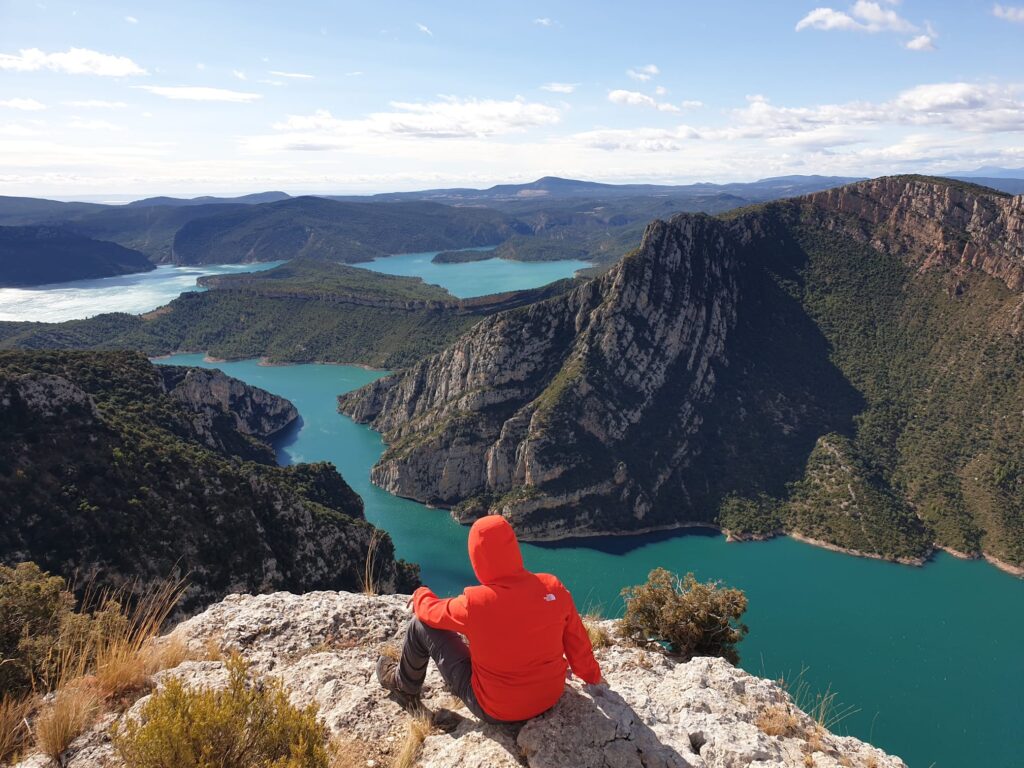 Persona contemplando un embalse turquesa desde lo alto en una ruta de senderismo