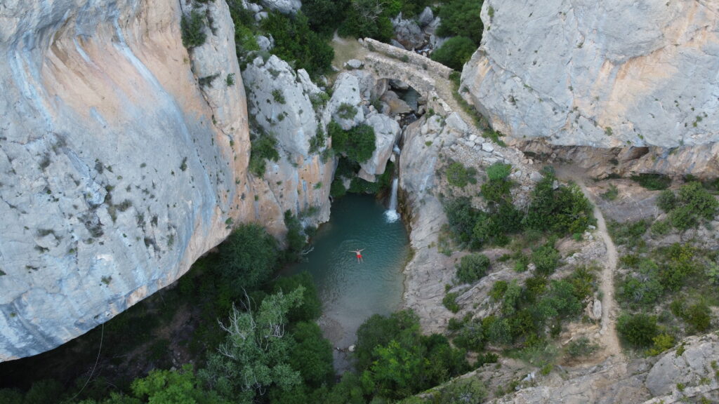 Vista aérea de la cascada de Bóixols con persona bañandose en la poza y puente medieval, Pallars Jussà